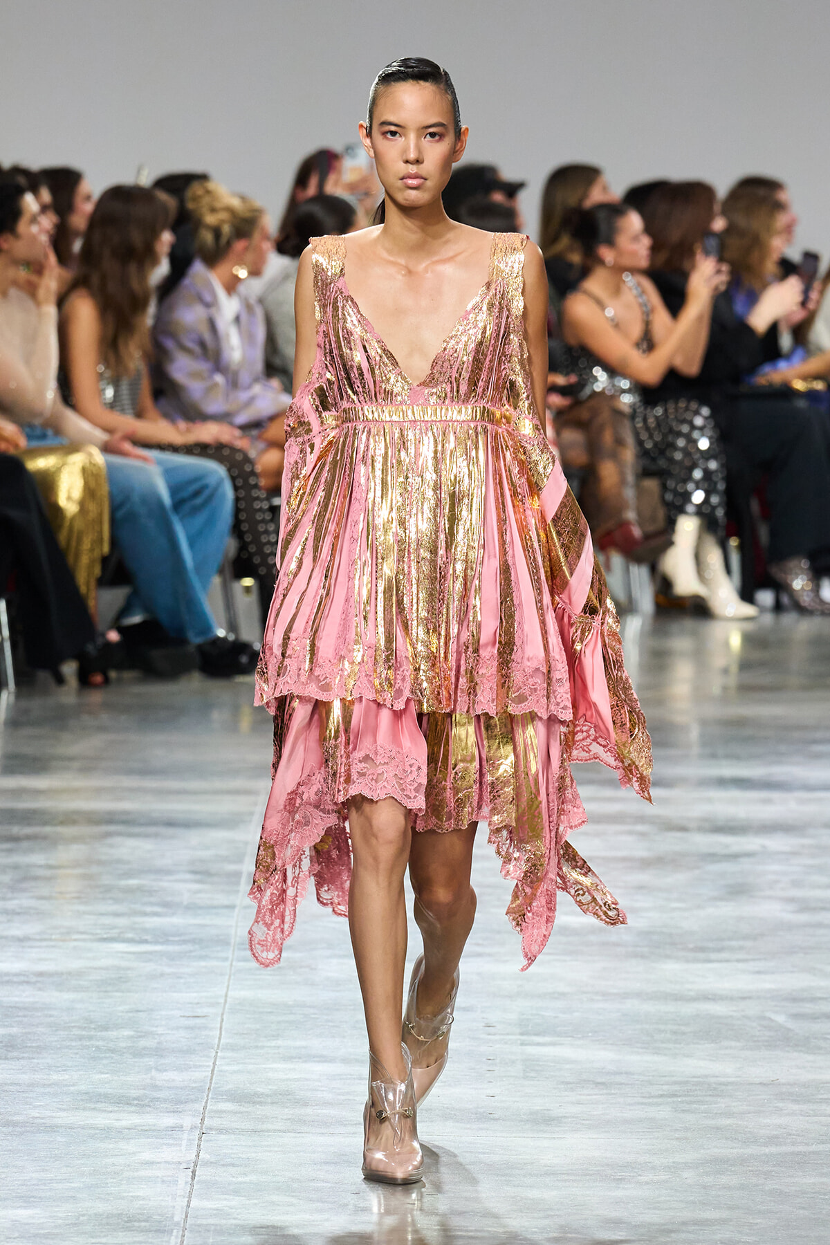 Model walking a pink and gold metallic gown with lace trim on a fashion runway