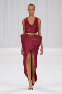 Model walks the runway in a magenta sequined sleeveless dress with a wide gold belt.