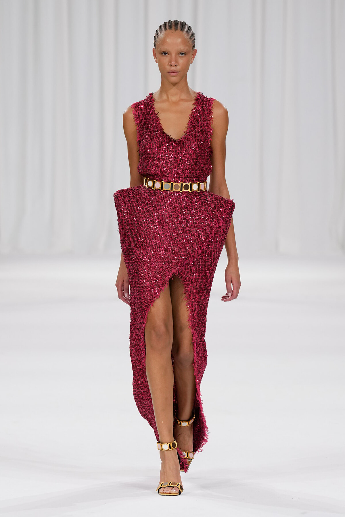 Model walks the runway in a magenta sequined sleeveless dress with a wide gold belt.