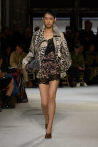 Model on a runway wearing a beige leopard-print oversized jacket over a pink lace mini dress, carrying a patterned bag.