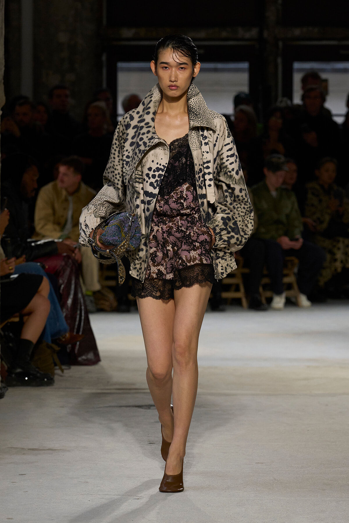 Model on a runway wearing a beige leopard-print oversized jacket over a pink lace mini dress, carrying a patterned bag.
