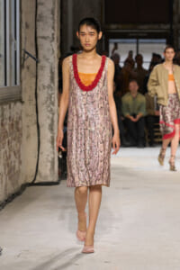 Model walking the runway in a pink snakeskin slip dress with orange underlayer and a red beaded neckline; audience in background.