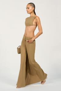 Model in a tan crop top and wide-leg pants, walking in a studio while holding a small tan handbag.