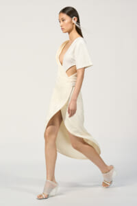 Model in an ivory wrap dress with side cutouts, walking forward in white heeled sandals.