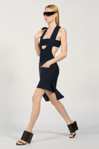 Model walking in a navy cutout midi dress with wide straps, paired with oversized black sunglasses and chunky black platform sandals.