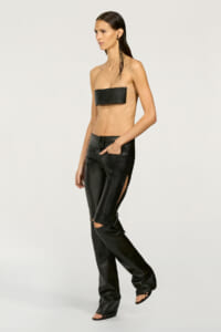 Model wearing a black bandeau-style top and matching black leather pants with side slits, posing in a studio.