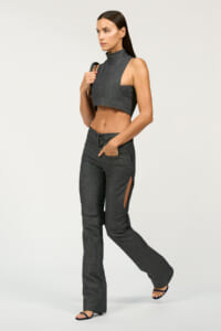 Model wearing a dark denim sleeveless cropped top and matching high-waisted jeans with side slits, walking forward with a bag strap over her shoulder.