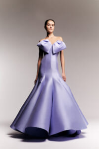 Woman wearing a lavender off-shoulder ball gown with a large bow at the neckline and a full, satin skirt.