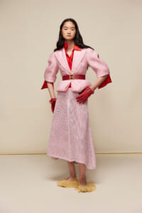 Model in pastel pink blazer over red blouse, cinched with a red belt, and a pink crochet midi skirt with red gloves.