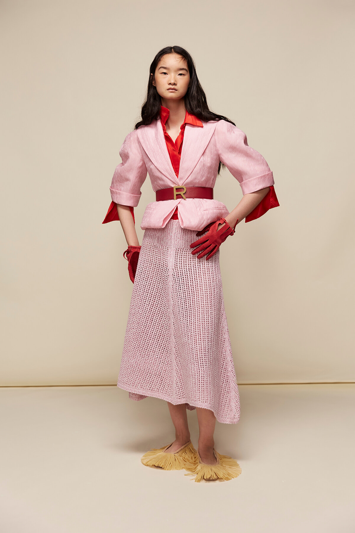 Model in pastel pink blazer over red blouse, cinched with a red belt, and a pink crochet midi skirt with red gloves.