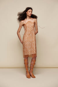 Model wearing a sheer peach dress with orange floral embroidery and matching tan gladiator sandals.