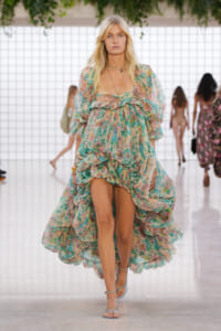 Model walking the runway in a pastel floral print dress with a voluminous, ruched skirt and matching sandals.