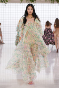 Model walking the runway in a pastel floral, billowy gown with sheer, flowing layers.