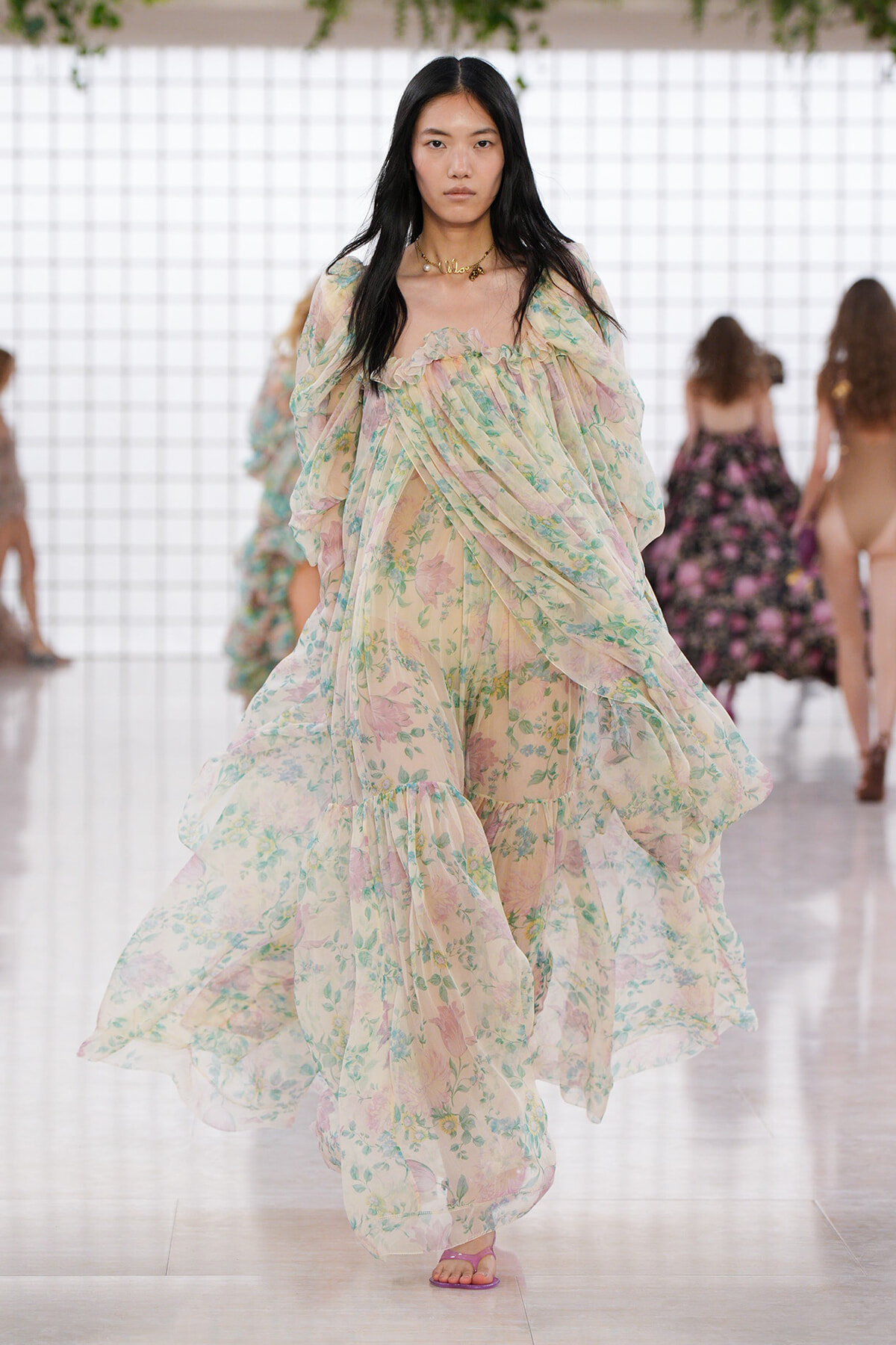 Model walking the runway in a pastel floral, billowy gown with sheer, flowing layers.