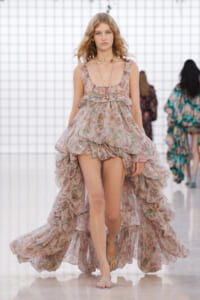 Model walking the runway in a pink floral, layered high-low dress with ruffles.