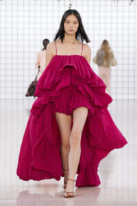 Model walks the runway in a vivid magenta, multi-layered ruffled gown with thin shoulder straps.