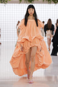 Model walks the runway in a voluminous peach off-the-shoulder gown with pink strappy sandals.