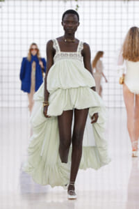 Model walks the runway in a pale mint green oversized gown with a lace-trimmed bodice and voluminous layered skirt.