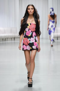 Front-facing model walks runway in a strapless black mini dress covered with large pink and red flowers.