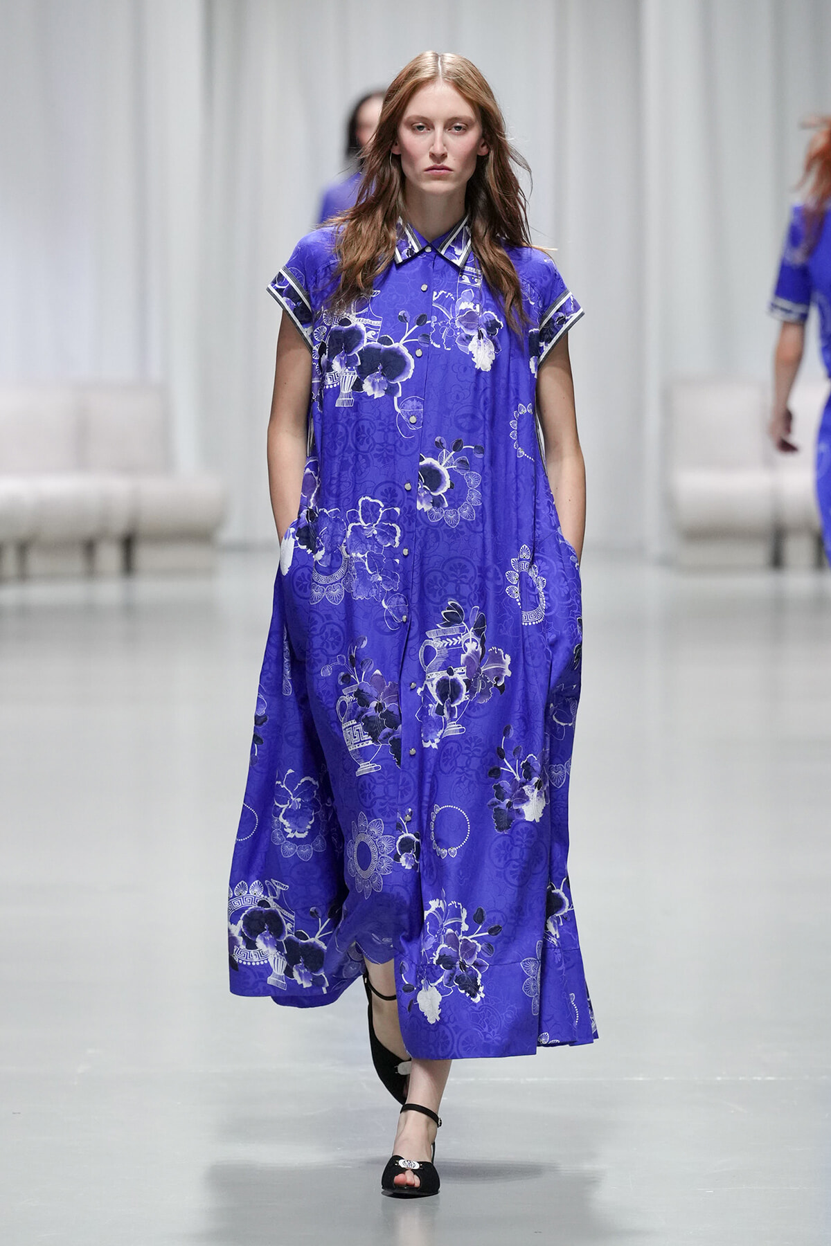 Model walking a fashion runway in a cobalt blue floral maxi dress with short sleeves and pockets.