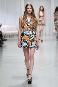 Model walking the runway in a sleeveless, multi-color floral-print mini dress with a belt and black platform sandals.