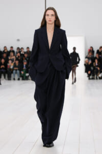 Female model walks a fashion runway in a dark pinstripe oversized suit with blazer and wide trousers.