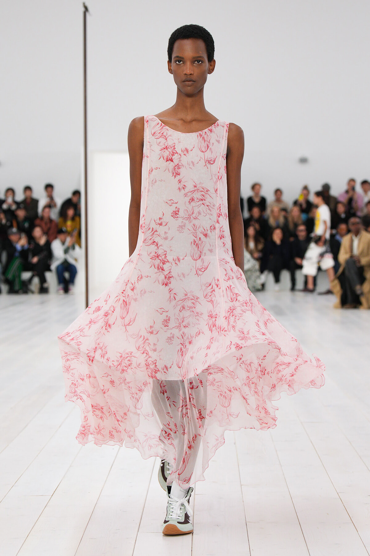 Model walking a fashion show wearing a light pink floral sleeveless dress that flows as she moves.