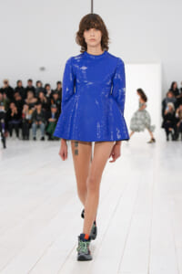 Model walking a runway in a bright royal blue sequined mini dress with long sleeves, wearing chunky sneakers.