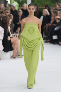 Model walks the runway in a lime-green strapless jumpsuit with a circular chest cutout and draped fabric.