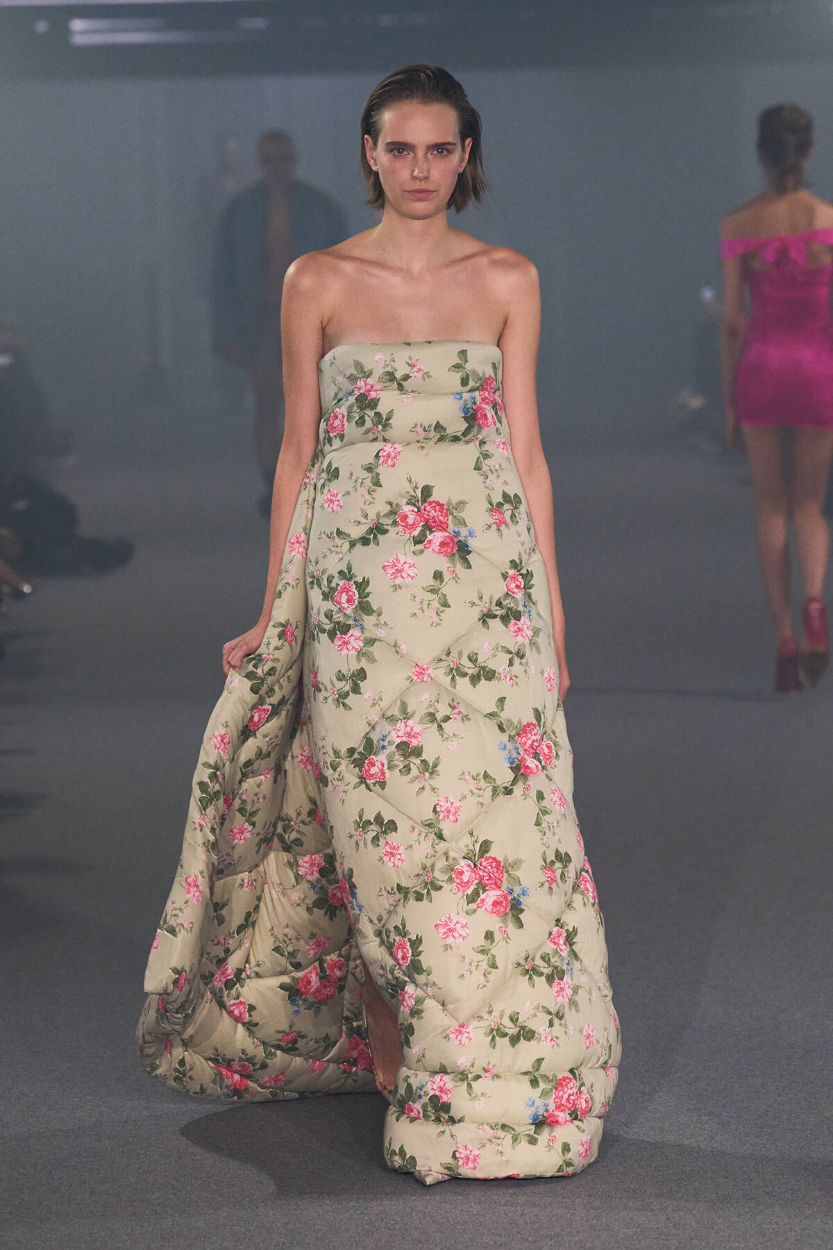 Model walks the runway in a strapless beige floral gown with a quilted, voluminous skirt.
