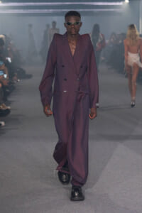 Male model walks the runway in an oversized purple double-breasted suit with black shoes and sunglasses.