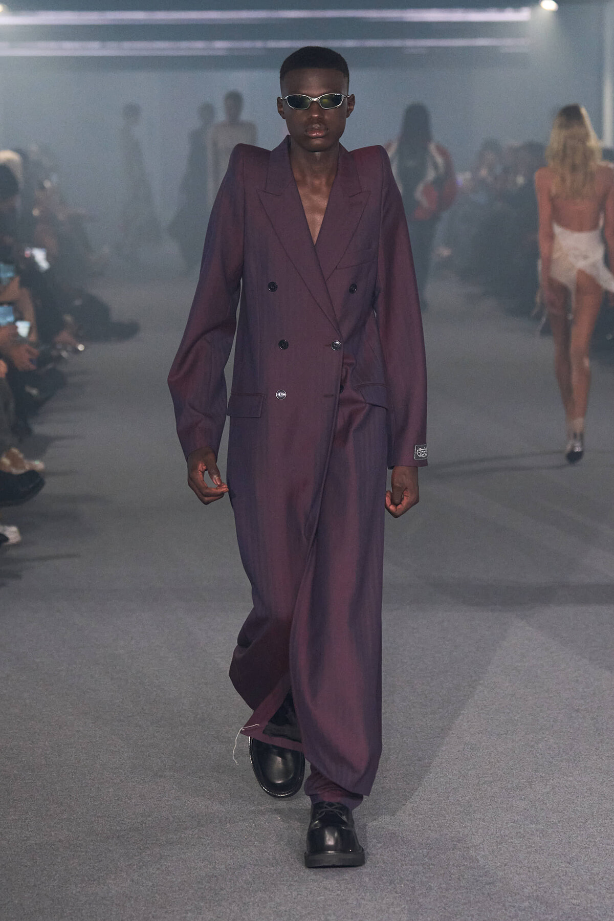 Male model walks the runway in an oversized purple double-breasted suit with black shoes and sunglasses.