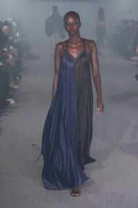 Model walks the runway in a two-tone gown: blue satin on one side and black on the other, with thin straps and a flowing, asymmetric skirt.