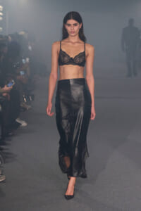 Model walks the runway in a black lace bralette and a floor-length black leather skirt with a front slit.