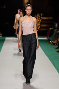 Model on a runway wearing a pale pink strapless bodice and wide-leg black trousers