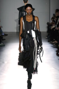Female model on a runway wearing an industrial, strap-filled black-and-white outfit with buckles and utility pockets.
