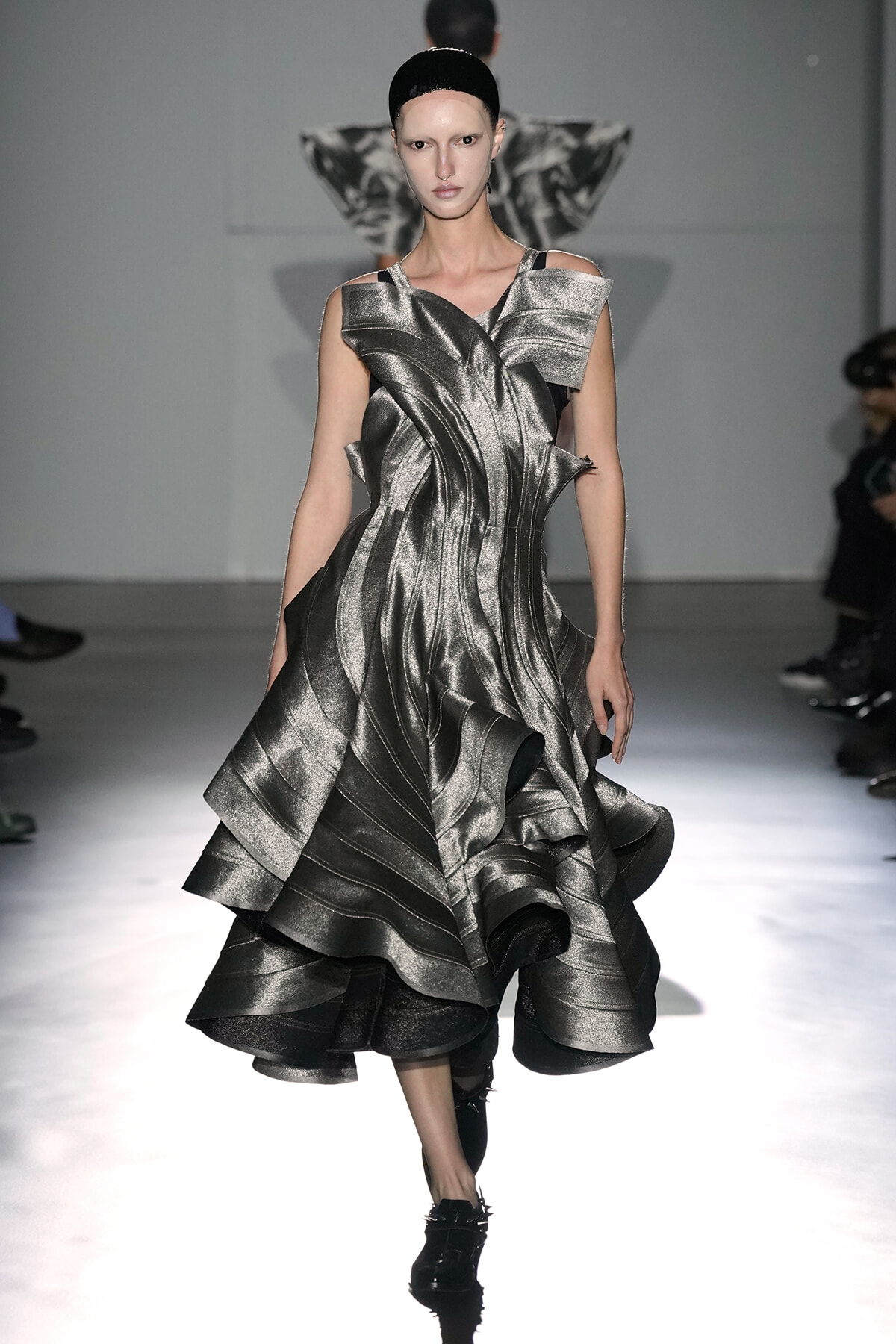Model on runway wearing a metallic silver sculptural gown with layered ruffles and a structured silhouette.