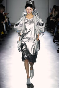 Model walking a silver metallic dress with oversized puff sleeves and matching gloves on a runway, futuristic look.