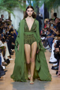 Model walks the runway in an olive-green, sequined plunging bodysuit with a matching long cape.