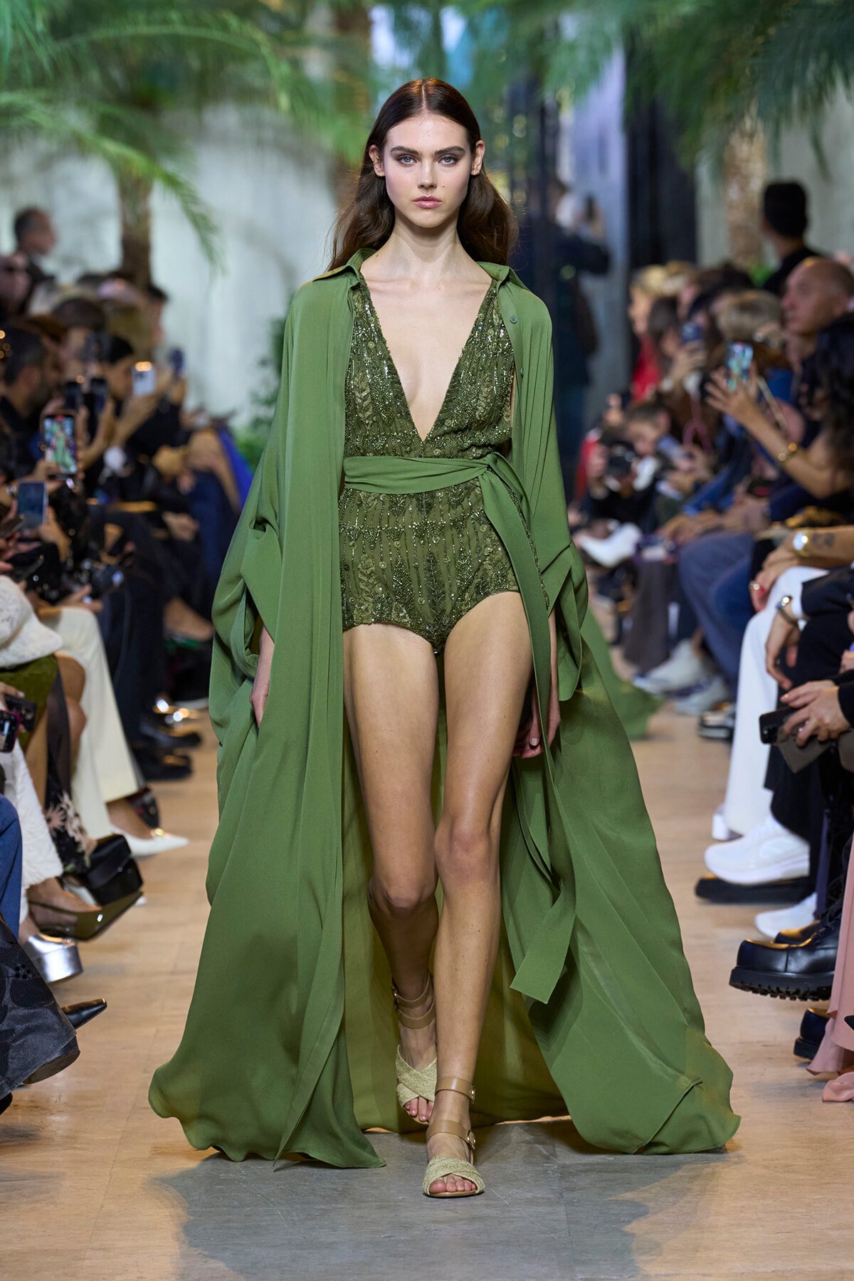 Model walks the runway in an olive-green, sequined plunging bodysuit with a matching long cape.