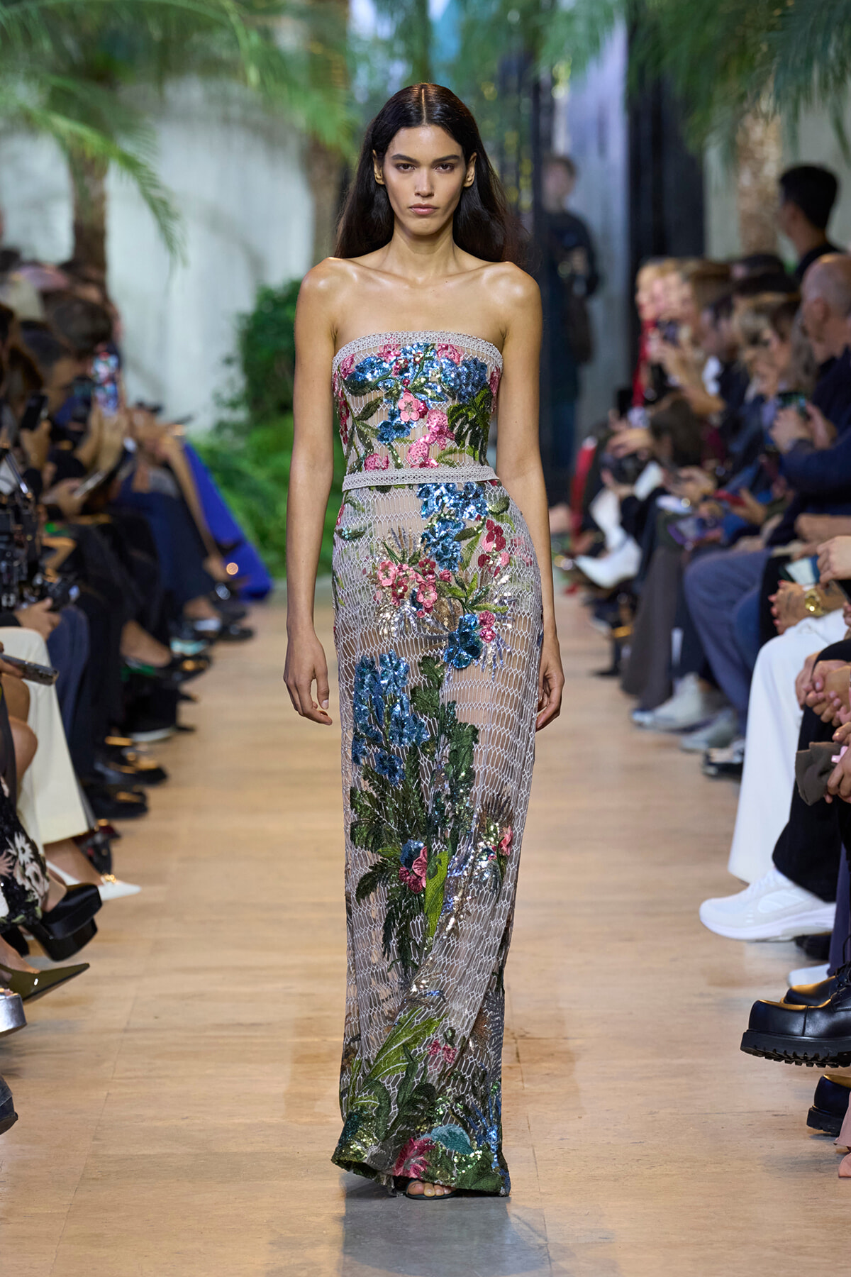 Model walks the runway in a strapless, floor-length gown covered in colorful floral sequins and a mesh overlay.
