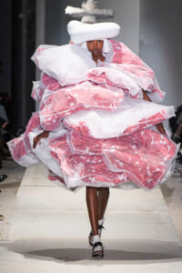 Model walks the runway in a voluminous pink and white sculptural gown with a white headpiece.