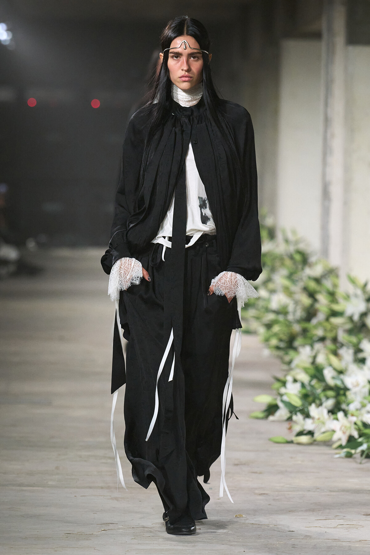 Model walking a fashion runway in a loose black ensemble with white accents and lace cuffs.