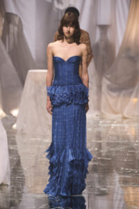 Model walking the runway in a strapless, cobalt-blue gown with a ruched bodice and dramatic layered ruffle skirt.