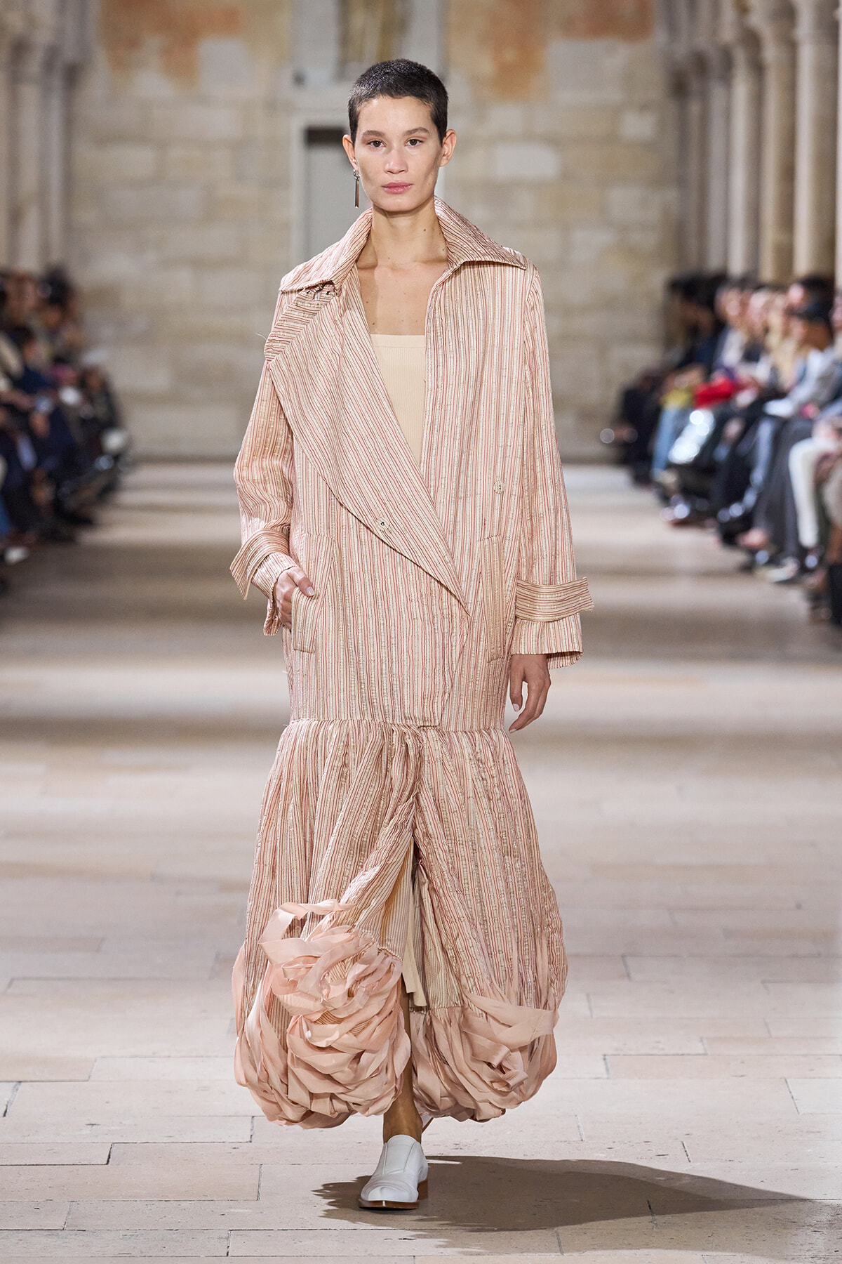 Model walking a fashion show in a pale pink striped coat with an oversized collar and a ruffled, balloon-like hem.