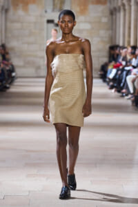 Model wearing a beige strapless mini dress with sheer ruffle layers, walking a runway.
