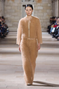 Model walks the runway in a beige textured zip-front jacket and matching wide-leg pants with a fluffy, fringe-like surface.