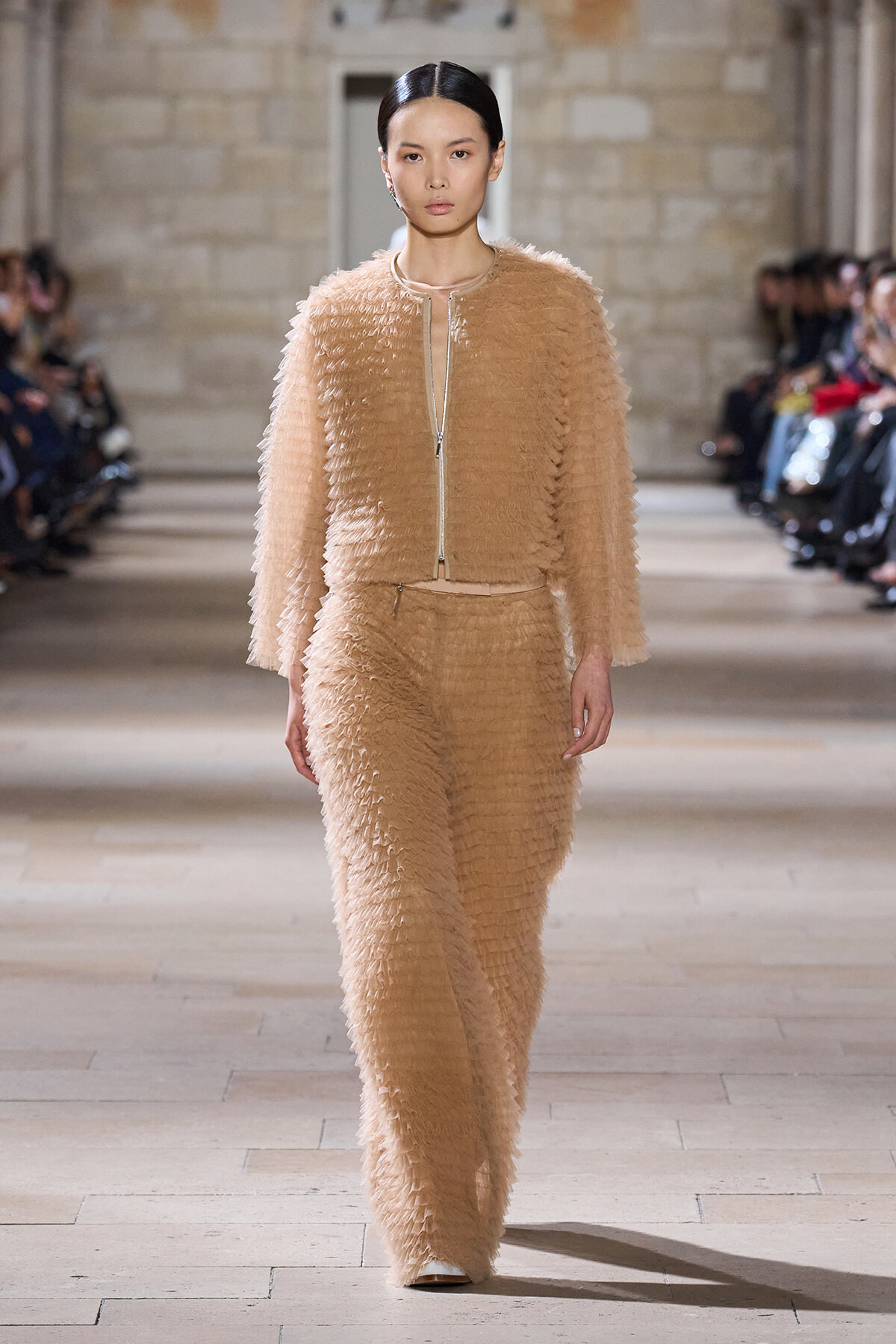 Model walks the runway in a beige textured zip-front jacket and matching wide-leg pants with a fluffy, fringe-like surface.