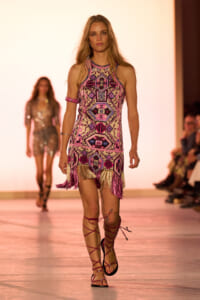 Model walking the runway in a pink geometric fringe mini dress with matching wrap sandal straps.