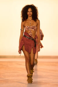 Model walking a runway in a strapless animal-print top and burgundy mini skirt with a chunky belt and tan boots.